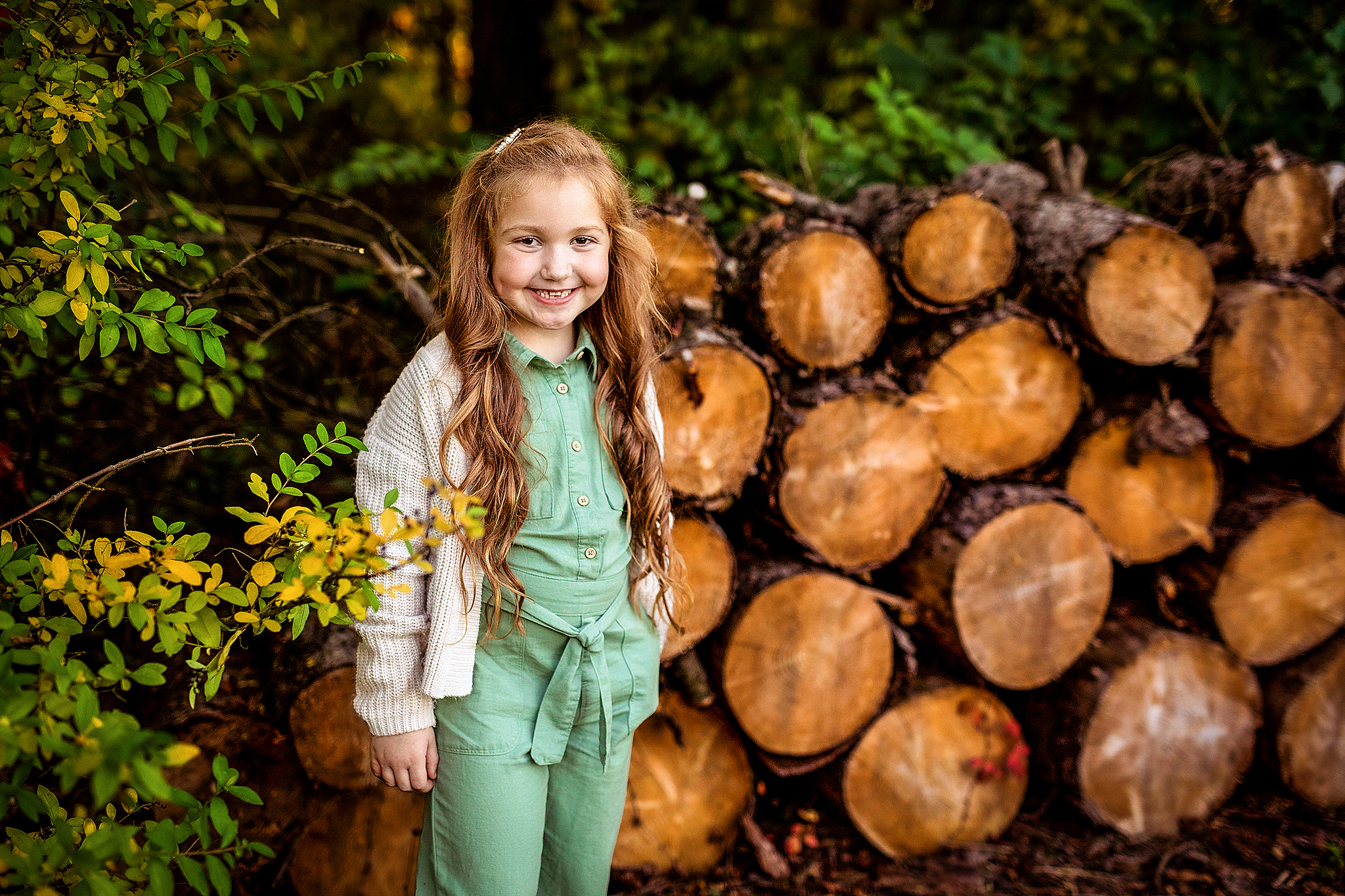 Young girl standing in front of a stack of logs.