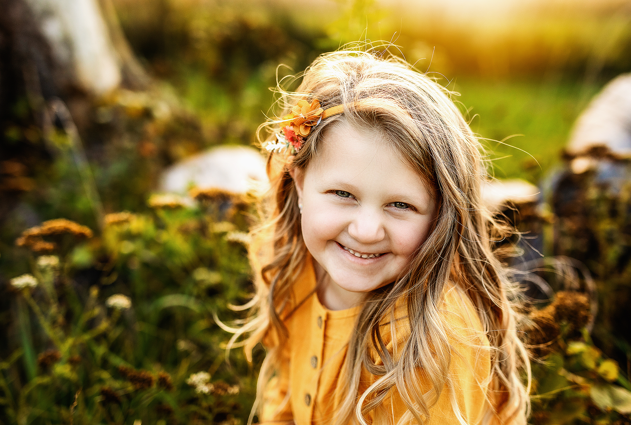 Young girl sitting on log and grinning in yellow dress