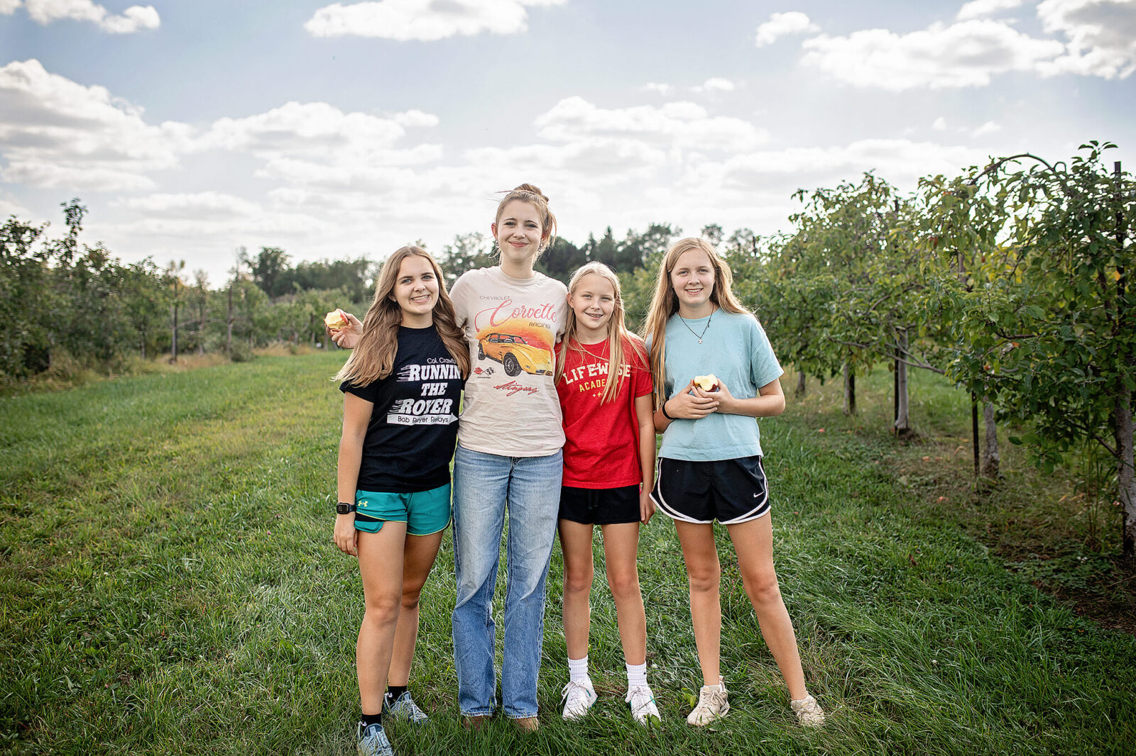 four sisters standing in apple orchard with apples in hand