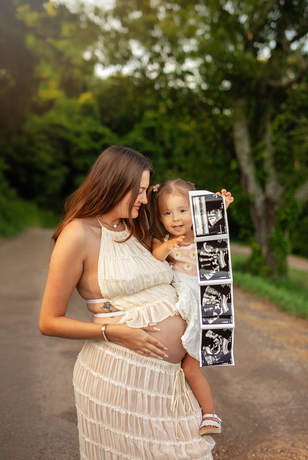 Pregnant mom holding toddler who is holding ultrasound photos of baby sister