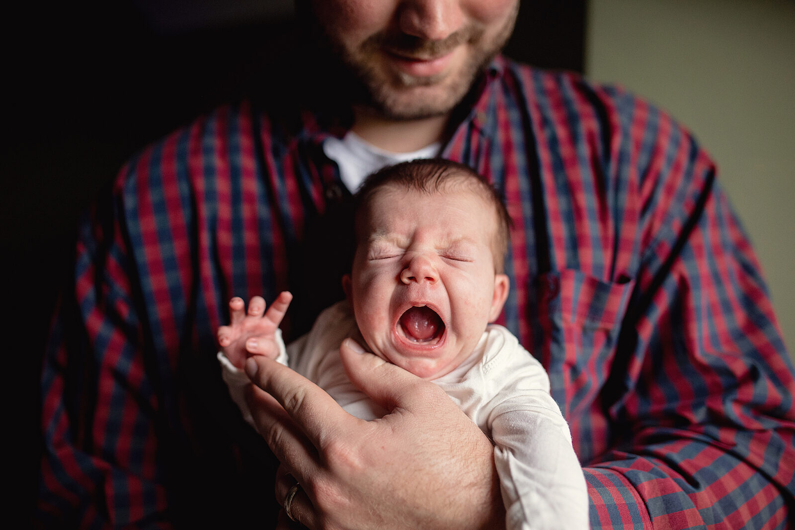 Newborn baby yawning while dad is holding baby in his hands in lifestyle session