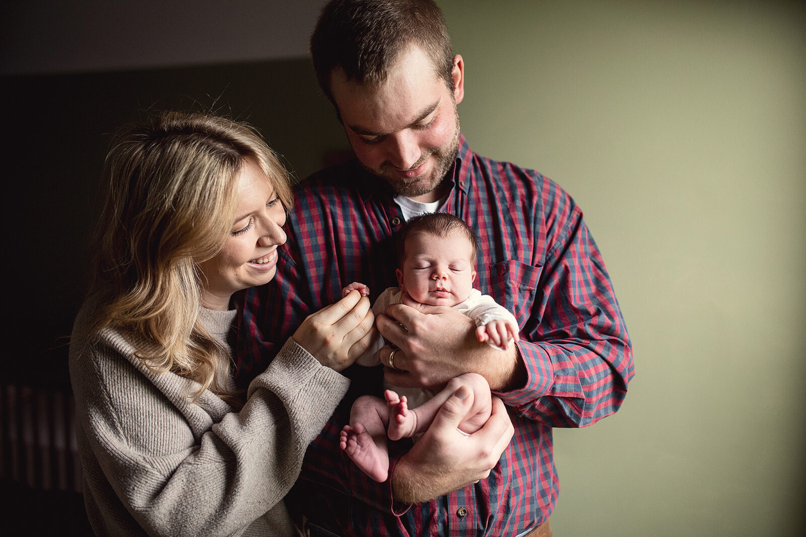Mom and dad holding newborn baby in front of window