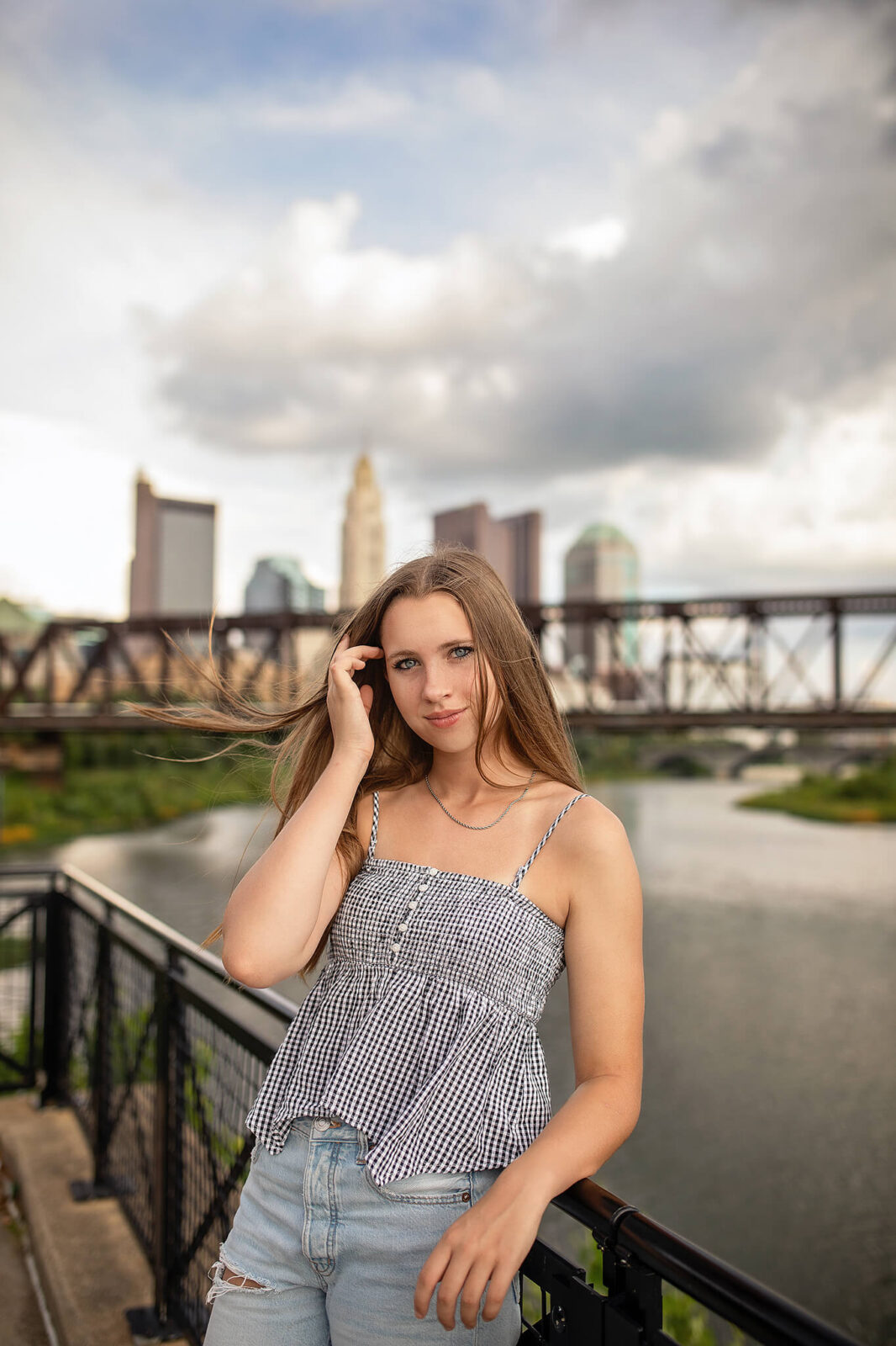 High school girl standing in front of water and columbus ohio skyline for senior photos