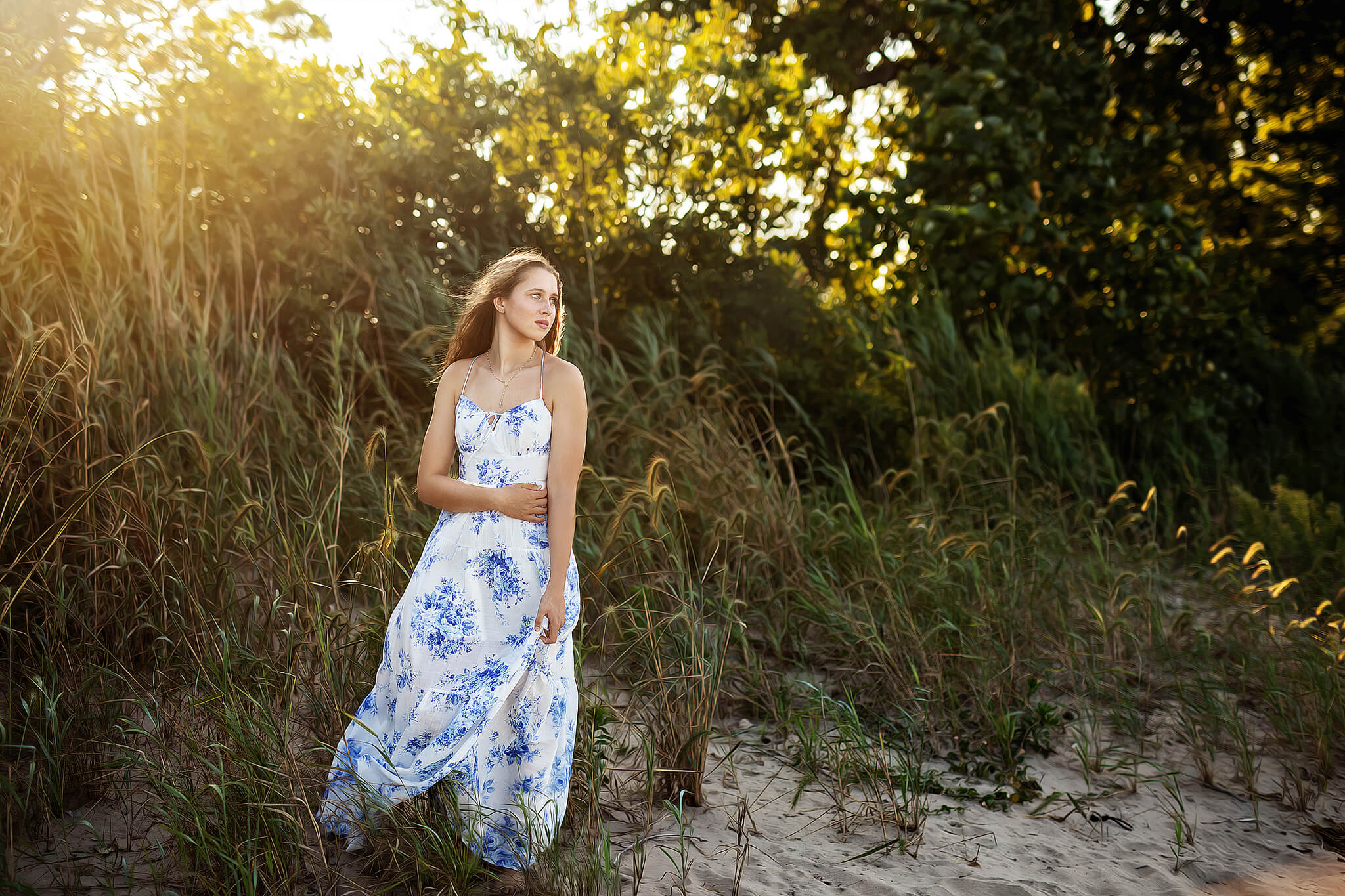 High school senior girl standing in beach grass with the beautiful sunlight behind her at East Harbor State Park