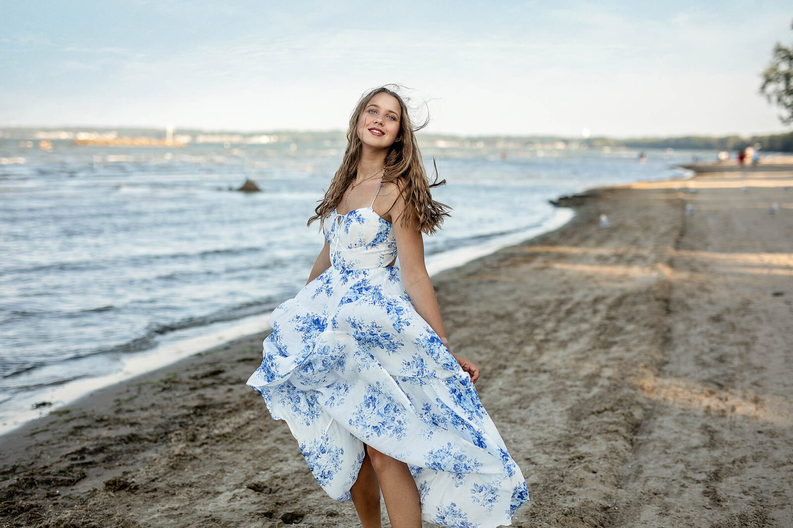 high school senior girl standing on beach with wind blowing her hair and dress at east harbor state park
