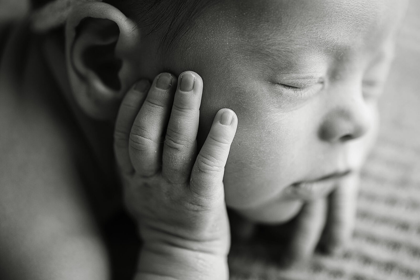 black and white image of newborn baby girl with her putting her hand to her cheek