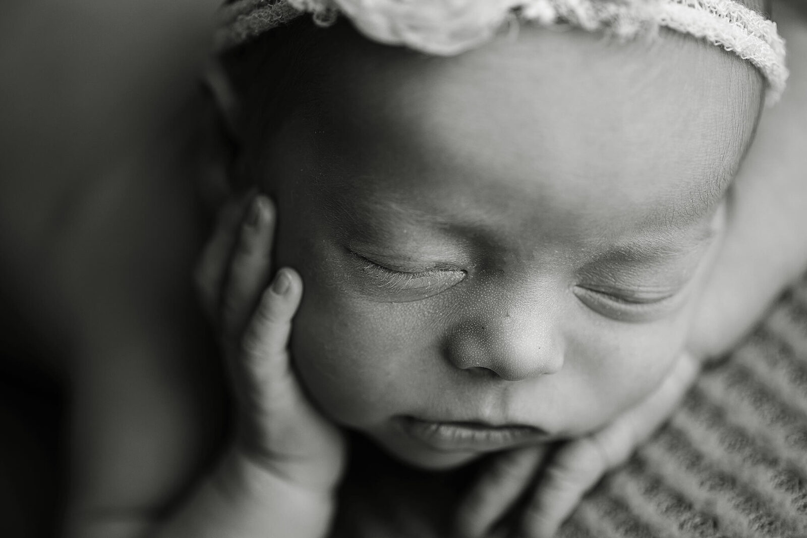 black and white image of a newborn touching her hand to her cheek in a close up